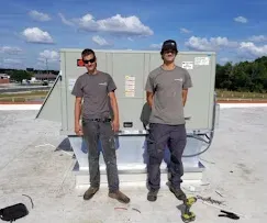 Two technicians standing beside a rooftop HVAC unit on a clear day.